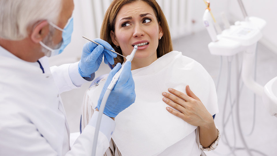 Zahnarztangst: Frau sitzt auf Behandlungsstuhl und hat Angst vor dem Zahnarzt, verzieht das Gesicht