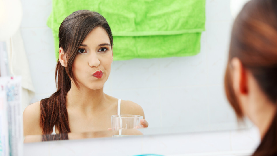 Eine Frau vor dem Spiegel benutzt eine Mundspülung