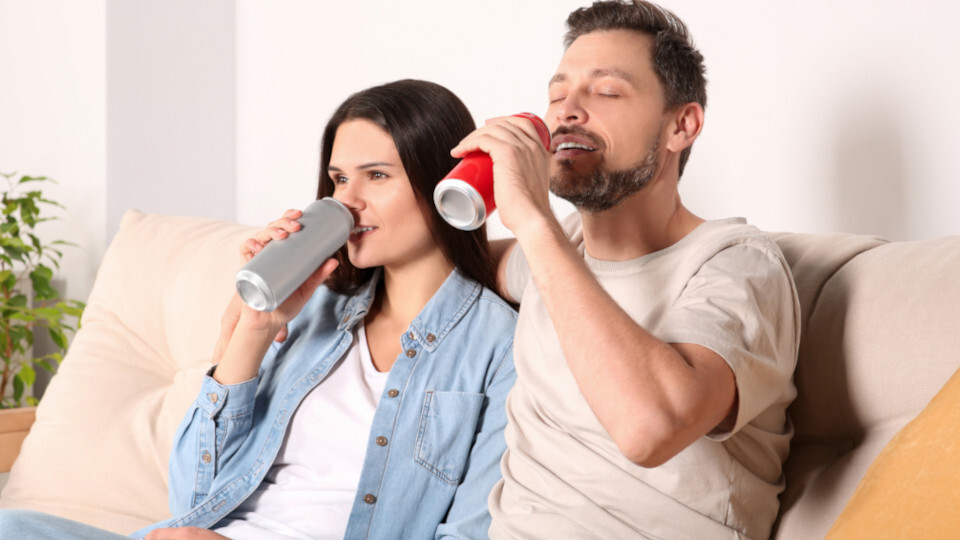 Ein Paar sitzt auf der Couch und trinkt Energydrinks